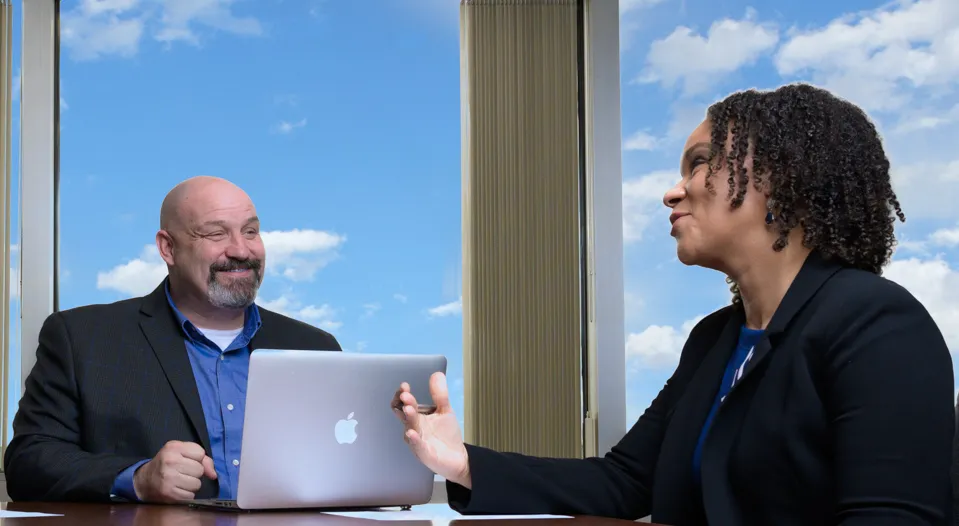 Two people at a table, engaged in discussion while using a laptop.